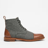 A side view of a men's ankle boot with a gray wool upper, brown leather toe cap and heel, black laces, and a wooden sole.
