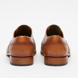 Rear view of a pair of brown leather dress shoes with brogue detailing and wooden soles.