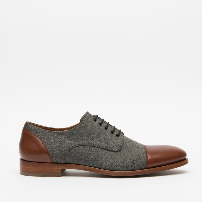 A side view of a grey felt and brown leather men's dress shoe with a lace-up design and wooden sole, displayed against a white background.