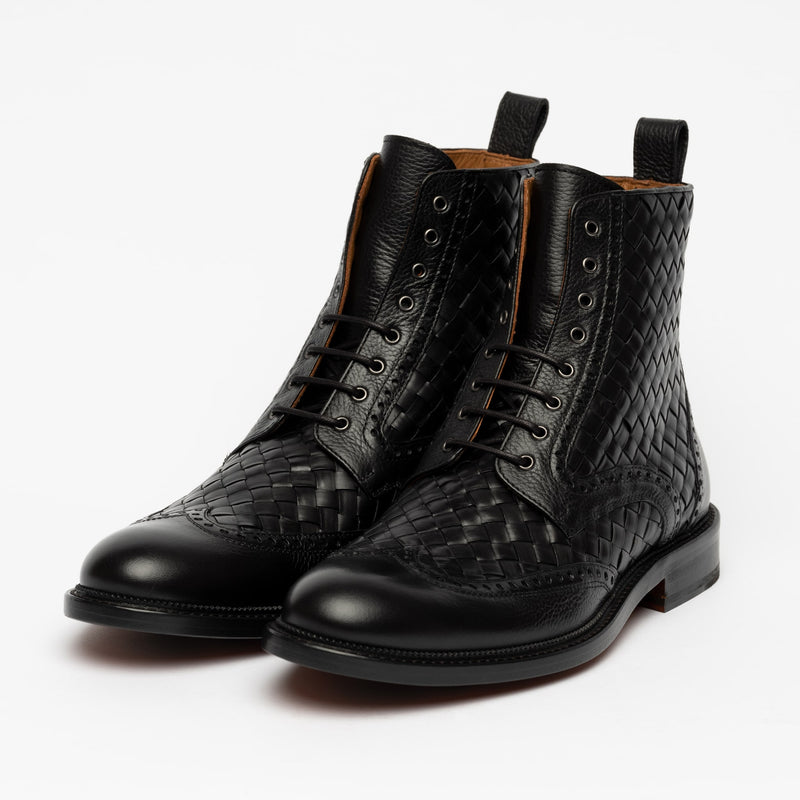 A pair of black woven leather lace-up boots with a polished finish, featuring brogue detailing and pull tabs, displayed against a white background.