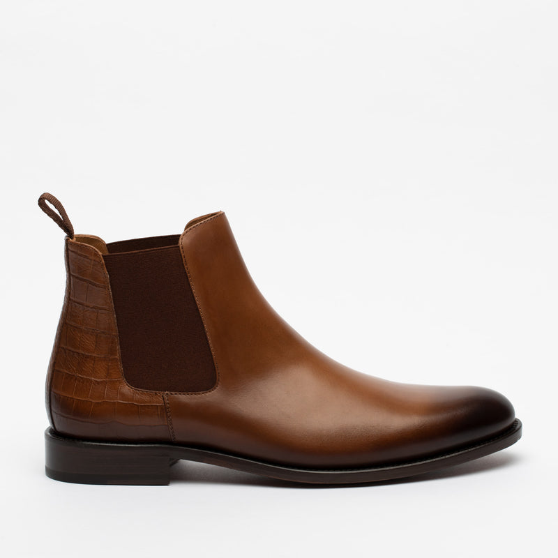 A single brown leather Chelsea boot with an elastic side panel and a pull tab, featuring a smooth finish on the upper and a textured pattern on the heel.