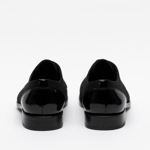 A pair of black formal shoes viewed from the back, showcasing sleek patent leather heels and a smooth, polished surface.