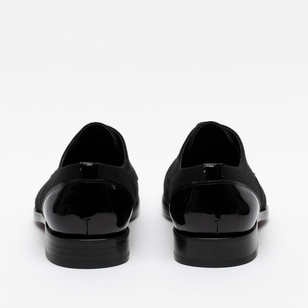 A pair of black formal shoes viewed from the back, showcasing sleek patent leather heels and a smooth, polished surface.
