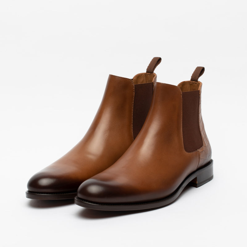 A pair of brown leather Chelsea boots with dark elastic side panels and pull tabs, photographed on a white background.