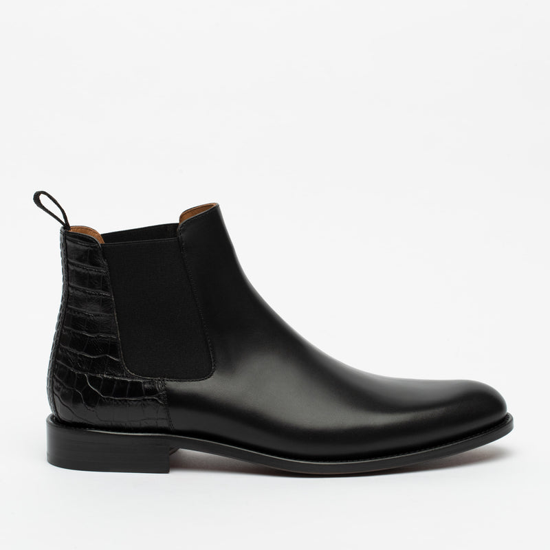 A black leather Chelsea boot with a crocodile texture heel and elastic side panels, shown against a white background.